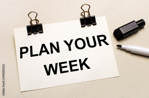 On a light background, a black open marker and on black clips a white sheet of paper with the text PLAN YOUR WEEK