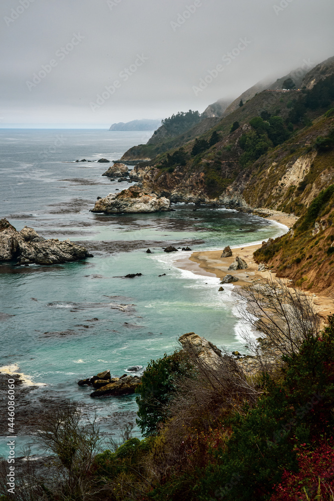 Pacific Ocean remote coastal area with rocks and sand beach with steep slope and fog along California shoreline