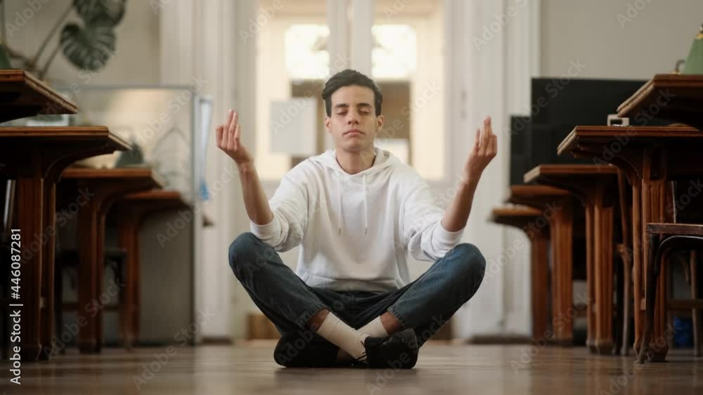 A calm arabian man with closed eyes is sitting in the yoga dzen pose on the floor in the hall A calm arabian man with closed eyes is sitting in the yoga dzen pose on the floor in the hall