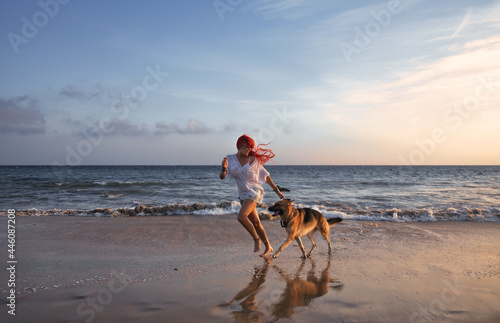Red-haired woman and her dog running free along the beach at sunset. Relax, fun, and enjoy summer vacation
