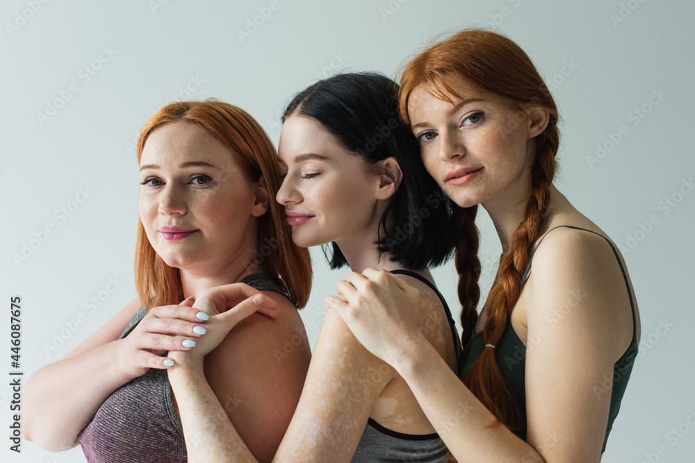 Pretty body positive sportswomen holding hands isolated on grey Pretty body positive sportswomen holding hands isolated on grey