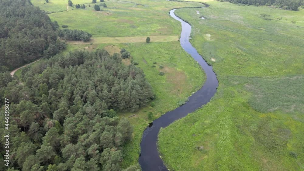 A view from above on the green meadows in the Narew river valley.The river is crossed by a road with a truss bridge on it.The valley is surrounded by forests. A view from above on the green meadows in the Narew river valley.The river is crossed by a road with a truss bridge on it.The valley is surrounded by forests.