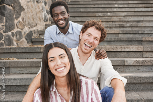 Young multiracial people sitting on stairs in the city while smiling on camera - Friendship and diversity