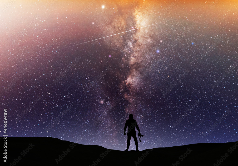 Fototapeta premium Beautiful starry night, man silhouette with a camera looking at the Milky Way galaxy. Night landscape, astronomical background.