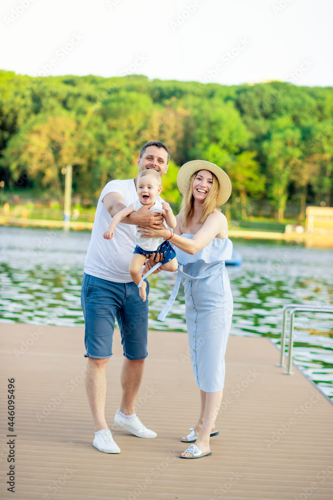 Fototapeta premium happy young parents mom and dad with their baby son walk in the summer by the water by the sea on the embankment and have fun, throwing the child up like a plane