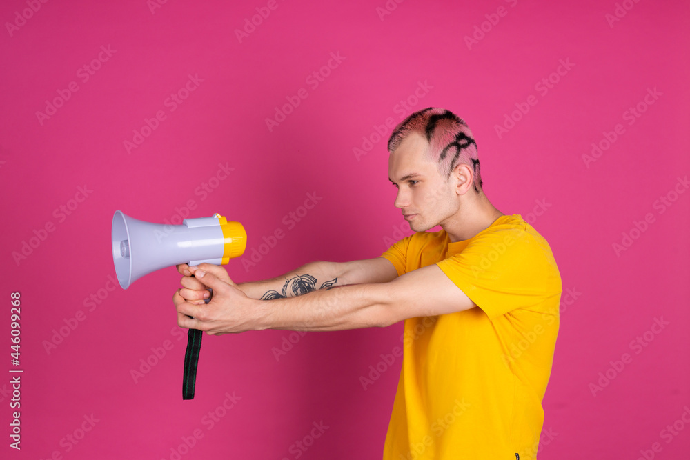 European handsome young man in yellow t shirt on pink background playing with megaphone as gun European handsome young man in yellow t shirt on pink background playing with megaphone as gun