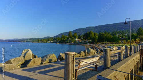 Dundarave pier on a summer morning with palm trees in park and Cypress mountain on right and view across Burrard Inlet bay
