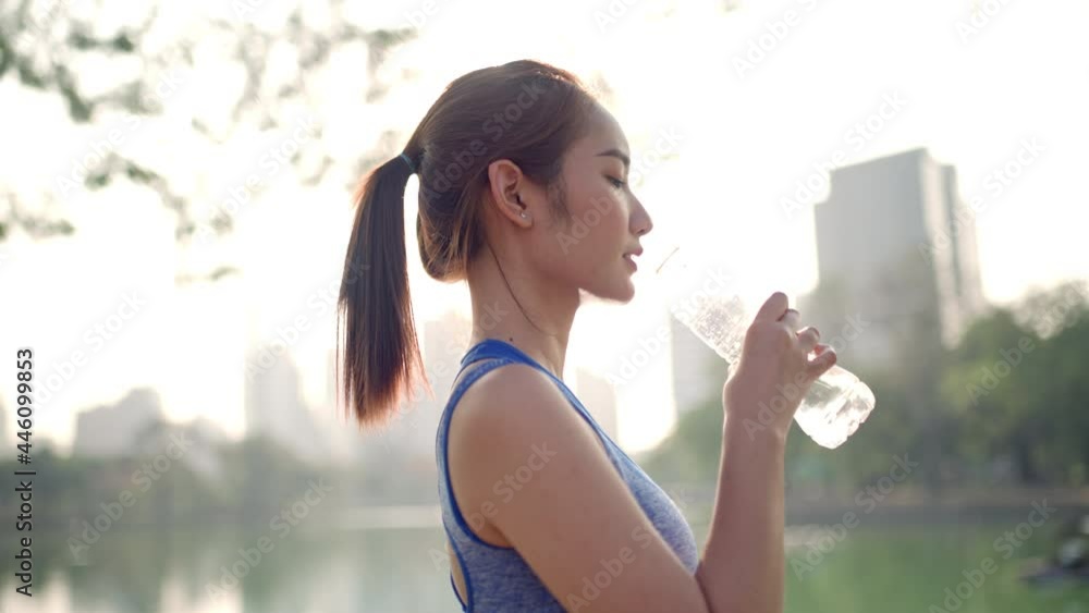 A woman is drinking water beside a pond in the city park 