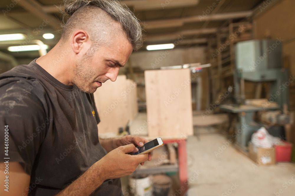 Carpenter artisan resting in workshop and scrolling on smartphone. Handsome handicraftsman texting message and tapping on phone Carpenter artisan resting in workshop and scrolling on smartphone. Handsome handicraftsman texting message and tapping on phone