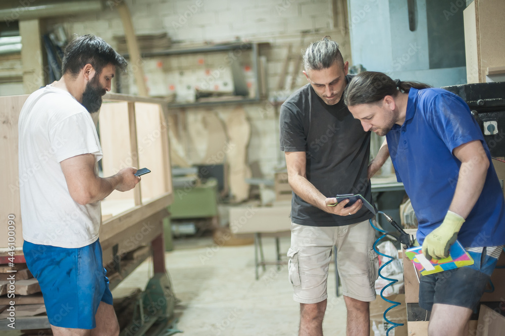 Carpenters resting in workshop and scrolling on smartphone. Handsome handicraftsman texting message and tapping on phone Carpenters resting in workshop and scrolling on smartphone. Handsome handicraftsman texting message and tapping on phone