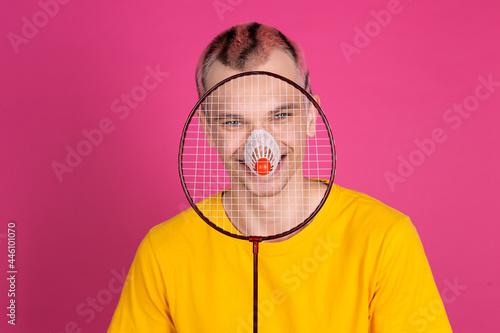 European handsome young man in yellow t shirt on pink background with badminton racket, sport concept © Анастасия Каргаполов