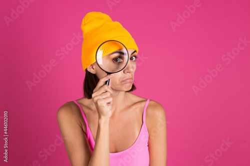 Bright portrait of woman in yellow hat on pink background with magnifier sad emotions © Анастасия Каргаполов