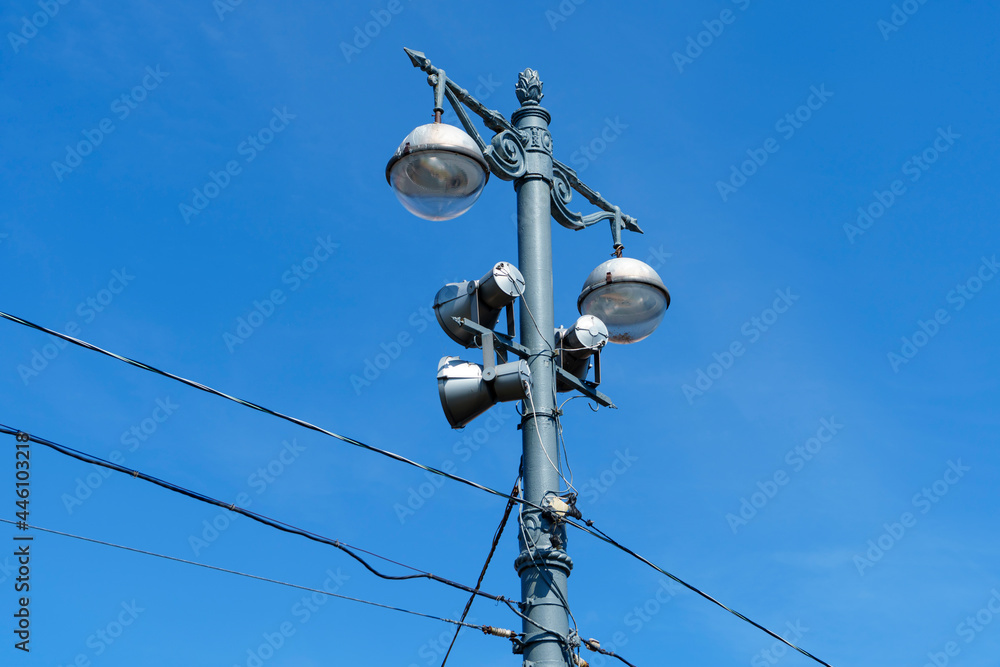 Old metal lampposts with street lamps and spotlights on blue sky Old metal lampposts with street lamps and spotlights on blue sky