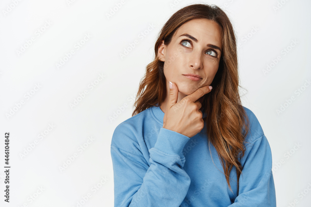 Hmm interesting. Portrait of brunette woman thinking, touching chin, looking aside thoughtful, ponder smth, making choice, standing against white background Hmm interesting. Portrait of brunette woman thinking, touching chin, looking aside thoughtful, ponder smth, making choice, standing against white background