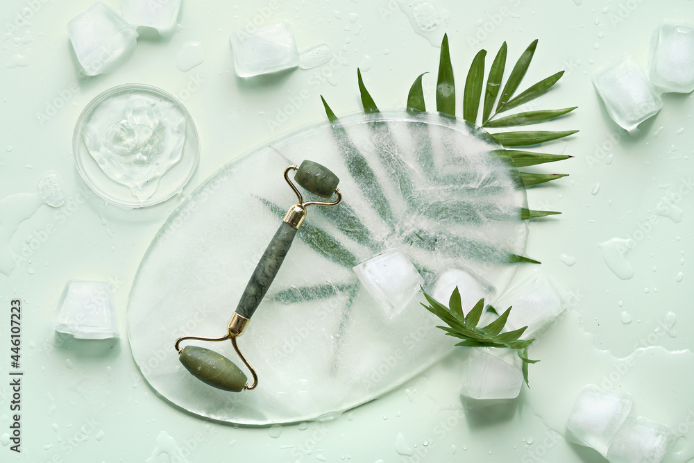 Obraz na płótnie Self made moisturizer and green jade face roller on oval piece of ice and ice cubes. Exotic palm leaves on mint green background. Minimal flat lay, top view. Facial massage, handmade cosmetics. w salonie