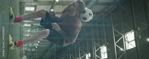 Vertical anamorphic shot of young Caucasian athlete juggling soccer ball while having workout on indoor field photo