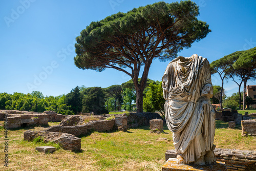 Ostia Antica, Rome Italy.Detail of a toga statue in the archaeological park site with brick architectural buildings from the imperial era, in summer with blue sky pine trees. Italy. photo