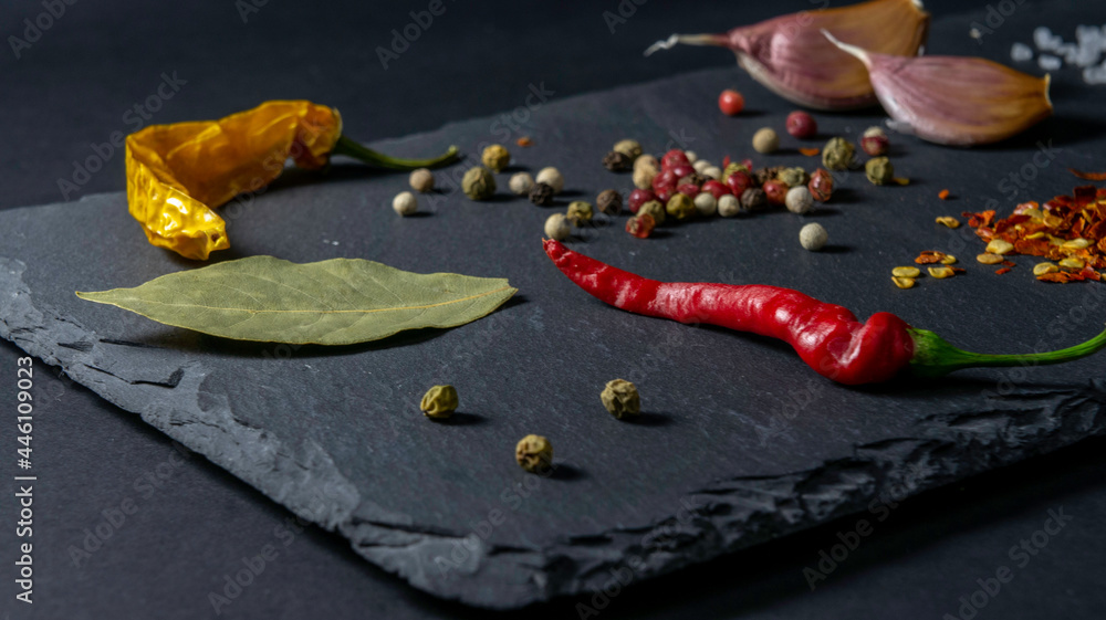 Spices on a stone plate. Black background. Black stone. Garlic, sea salt, pepper, chili, hot pepper, bay leaf