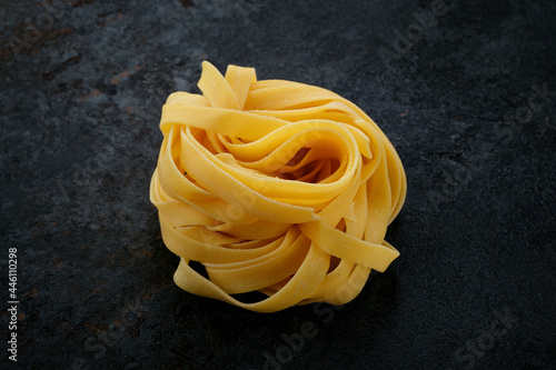 Natural Raw pasta tagliatelle on a black stone background. Fresh uncooked egg Italian pasta