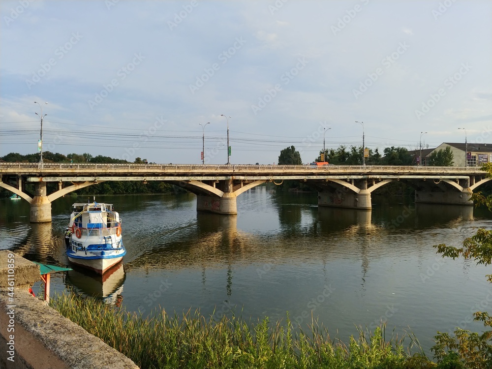 beautiful summer landscape with passenger boat docking on the river, concrete pedestrian bridge 