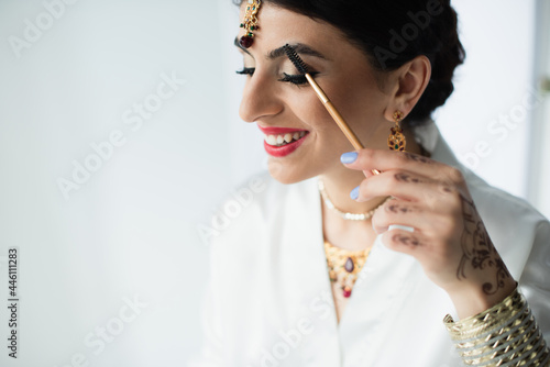 happy indian bride with mehndi styling eyebrow with cosmetic brush on white
