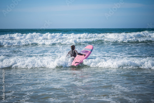 Girl with a surfboard overcomes the waves. Concept: Overcoming, Determination, Perseverance