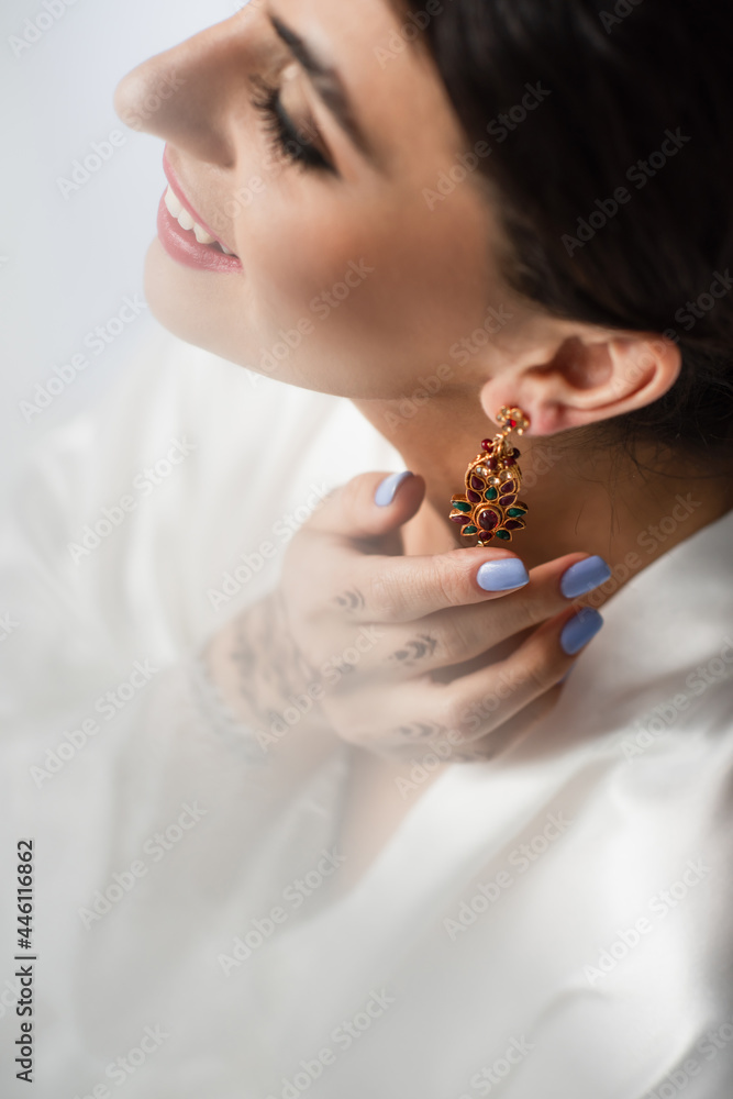 high angle view of happy indian bride wearing earring while getting ready for wedding isolated on white
