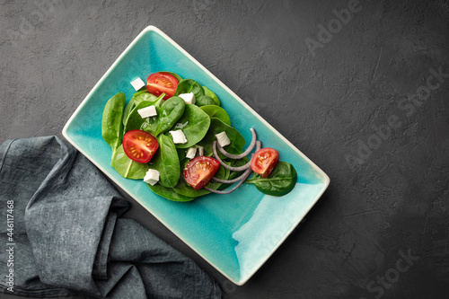Low-calorie spinach and tomato salad in a stylish plate. Top view. Black background.