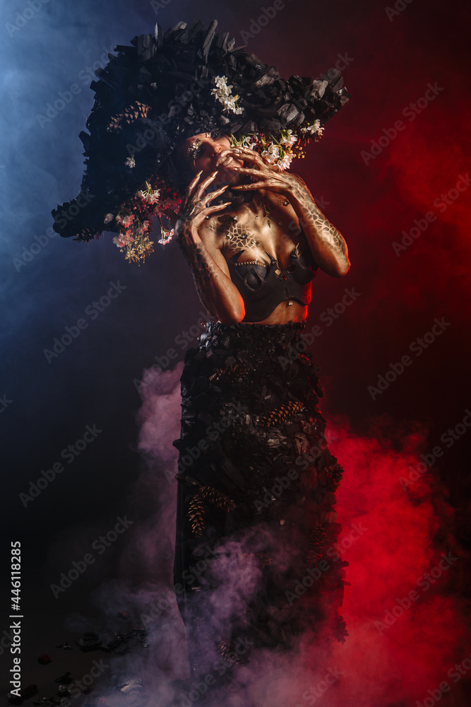 Portrait of a model in a headdress and dress made of coal. There is red smoke behind the model Portrait of a model in a headdress and dress made of coal. There is red smoke behind the model