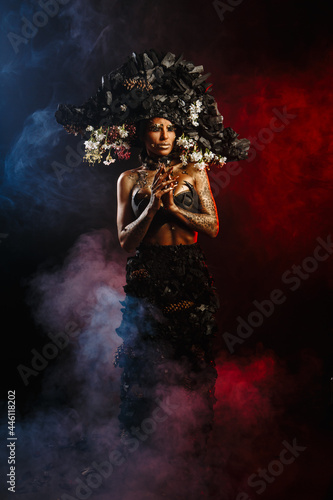Portrait of a model in a headdress and dress made of coal. There is red smoke behind the model