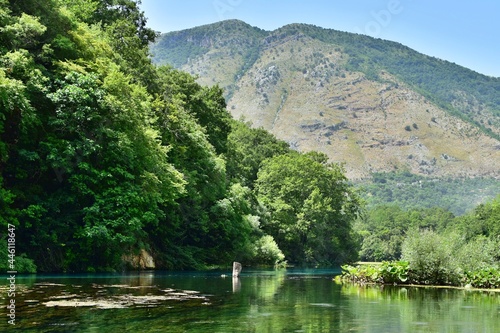 Crystal clear blue water of the river among green trees at foot of the mountain