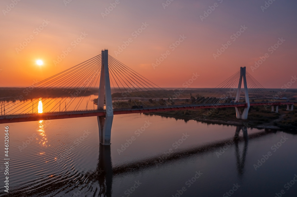 Obraz premium Aerial view of a white suspension bridge with two huge pillars above a river at sunrise in a rural area