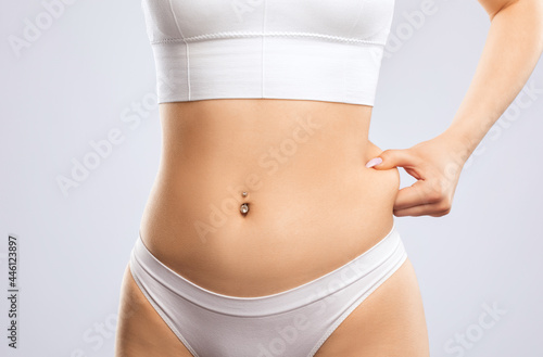 Girl pulls the skin on the abdomen, showing the body fat in the abdominal area and sides. Treatment and disposal of excess weight, the deposition of subcutaneous fat. © Dimid