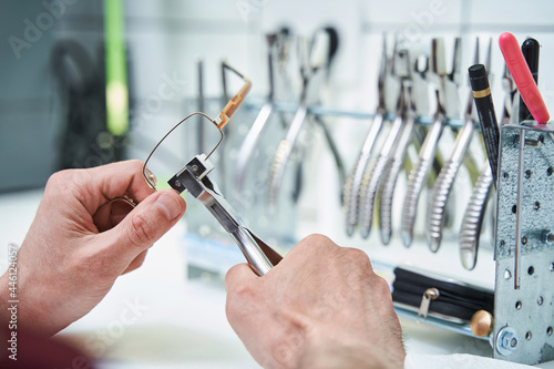 Male optician repairing glasses with pliers in workshop