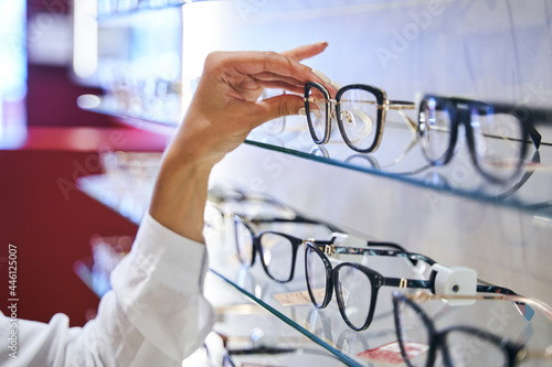 Female hand taking eyeglasses from shelf in optical store