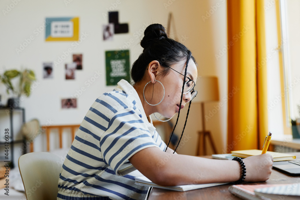 Side view portrait of Asian teenage girl studying at desk at home and ...