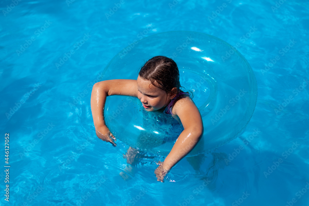 cheerful caucasian girl swims in the clear water of the sea hanging her hands on a blue inflatable circle, family sea vacation. 