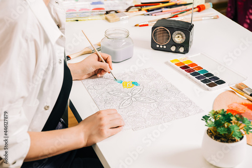 Young woman coloring page antistress at table indoors, mental wellbeing and art therapy. Woman paints a sketch, meditative process of coloring pages. Self expression by art