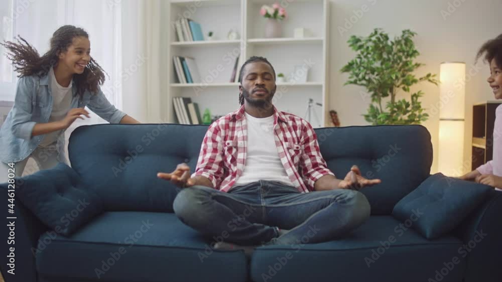 African father practicing yoga while daughters run around sofa, fatherhood African father practicing yoga while daughters run around sofa, fatherhood