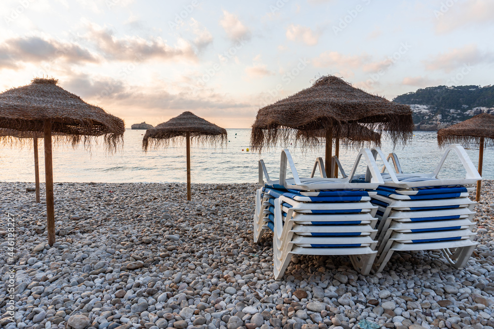 Empty beach at sunrise, with umbrellas and hammocks stacked in front of the Mediterranean Sea.