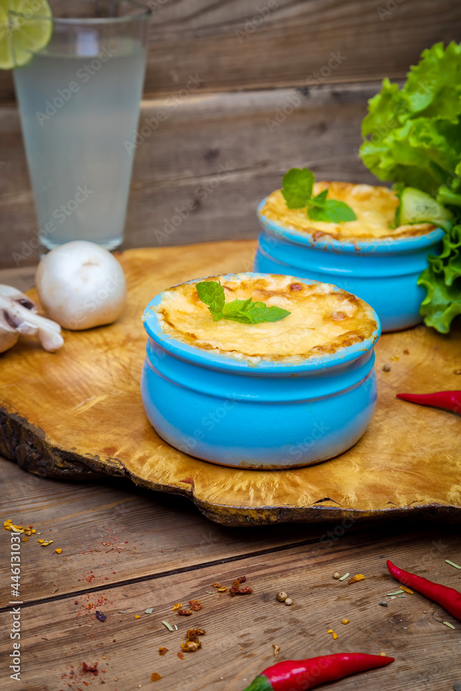 Pots with mushroom julienne on a wooden board, decorated with herbs. Julienne in cocotte with yellow cheese crust.