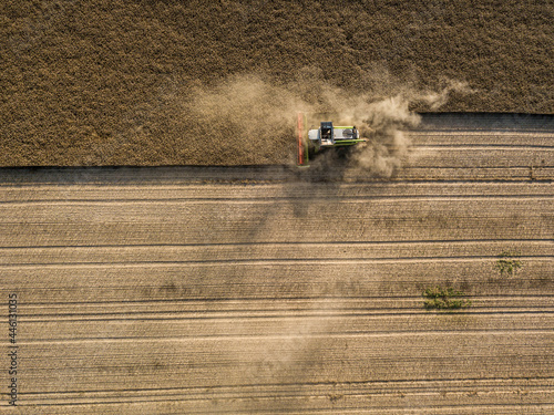 Drone shot of a combine harvester collecting canola on dry dusty farmland for a biofuel.