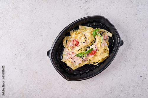 Tagliatelle carbonara in black plastic container on light background top view. Designer food concept for take away or delivery