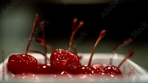 Photos shiny maraschino cherries with stems displayed in white bowl from side