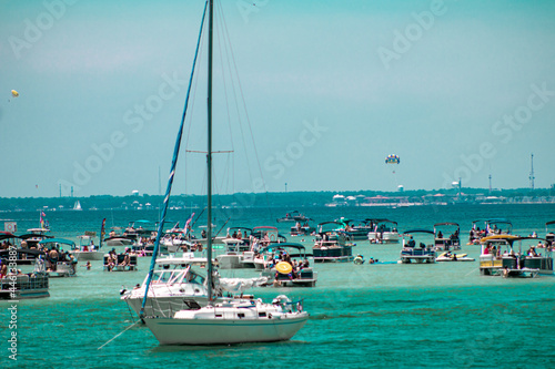 Variety of boats including sailboats parked, anchored off reef for boating party with turquoise water in Destin, Florida photo