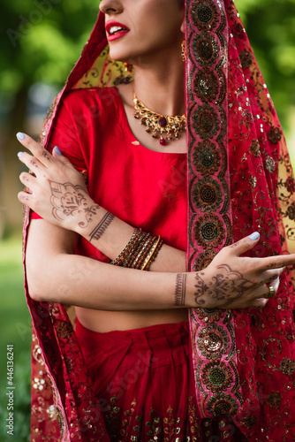cropped view of young indian bride in red sari and headscarf with ornament