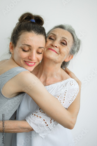 Happy senior mother is hugging her adult daughter, the women are laughing together, sincere family of different age generations having fun on white background, mothers day.