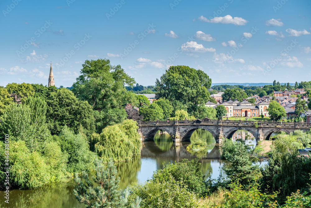 View towards the English bridge, Shrewsbury on a hot July day, with vibrant vegetation and light cloud on a blue sky. England, UK.
