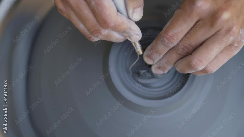 The manufacture of ceramics. Woman working with clay on pottery wheel. Bottom trimming excess clay and gloss the surface. Close up view of hands, view from above. The manufacture of ceramics. Woman working with clay on pottery wheel. Bottom trimming excess clay and gloss the surface. Close up view of hands, view from above.