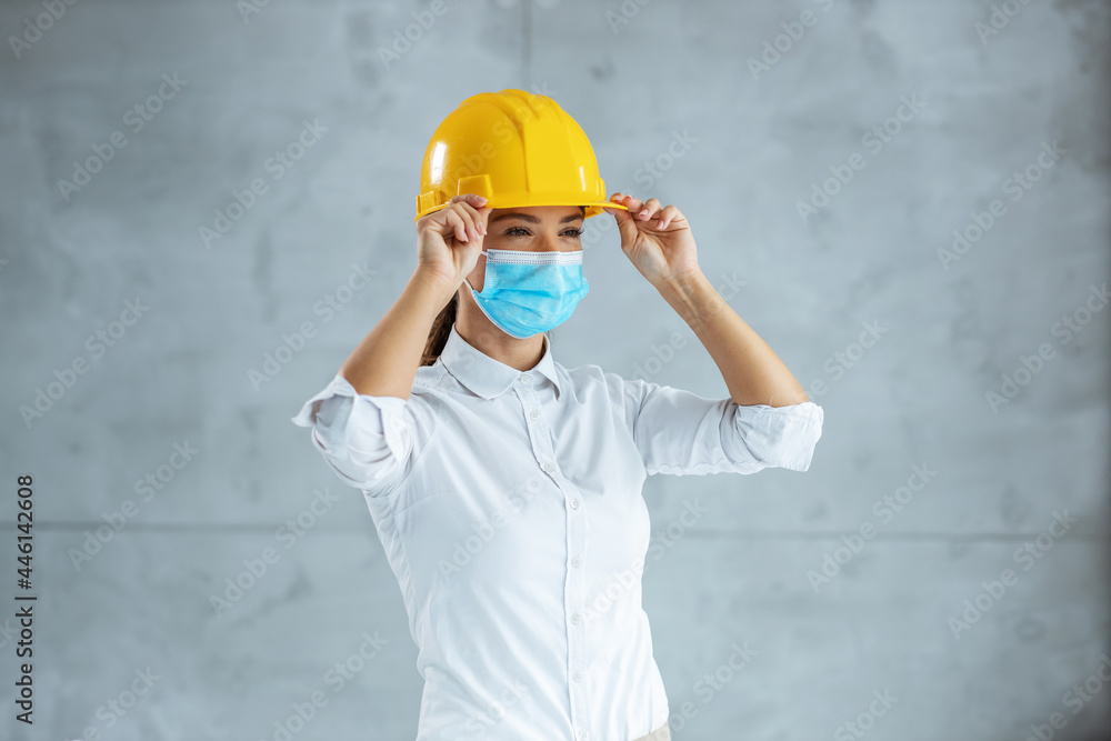 Female architect with face mask putting helmet on head and preparing to go on ste. Female architect with face mask putting helmet on head and preparing to go on ste.